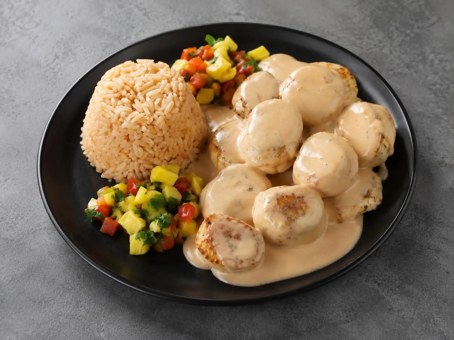 Metztli house chicken albondigas glazed in a chipotle-cream sauce, plated with Mexican rice and a bright mango pico de gallo