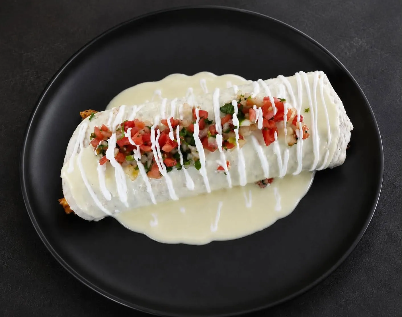 A burrito mojado at Metztli — flour tortilla smothered in queso, topped with pico de gallo and a drizzle of crema, on a black plate