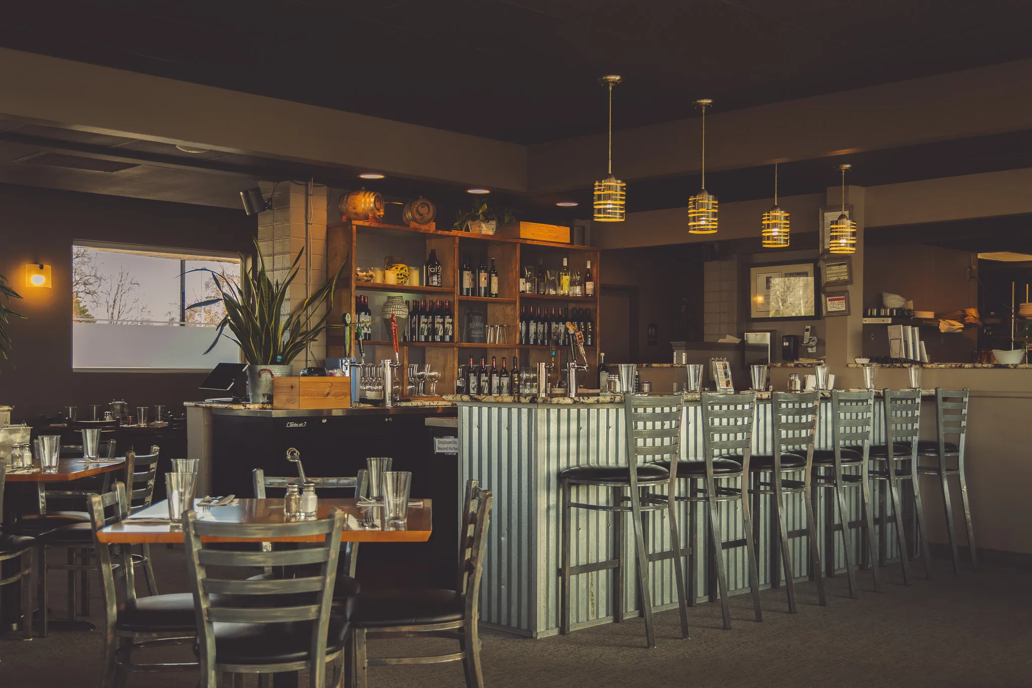 The bar at Metztli Cocina Bar with backlit tequila and mezcal bottles, amber pendant lamps, and a corrugated-metal bar front lined with steel chairs