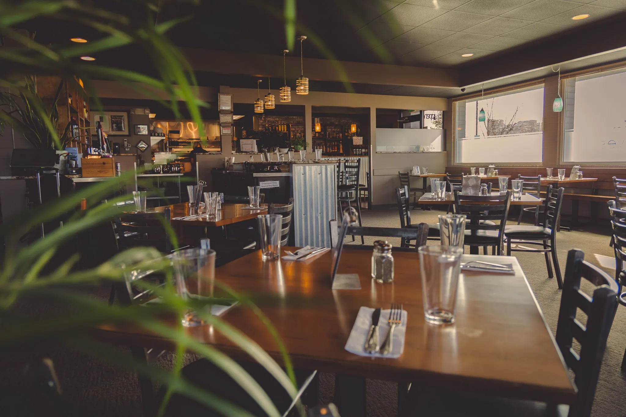 The Metztli Cocina Bar dining room in Richland — warm wood tables set with glassware, framed by tropical greenery and pendant lighting over the bar in the background